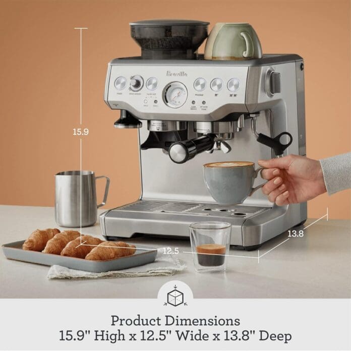A Breville Barista Express Espresso Machine is placed on a kitchen counter with a cup of coffee being prepared. The machine has a stainless steel finish, a built-in grinder on top, and various control knobs. A tray with croissants, a milk frothing pitcher, and a cup of espresso are also present. Dimensions of the machine are labeled as 15.9